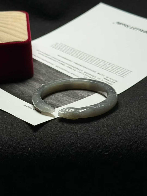 "Gelang ular" giok Hetian biru berasap - tekstur halus dan hangat, diukir tangan hingga tampak seperti aslinya. Ukuran perkiraan: 51 x 9 mm. Semua batu alam terbentuk secara alami; biaya pengiriman dan pajak sudah termasuk.