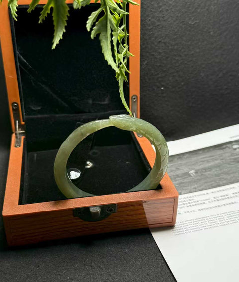 "Gelang Ular" giok Hetian ini memiliki rona hijau danau dan tekstur lembut yang hangat. Desain ukiran tangan yang tampak nyata. Perkiraan dimensi: 58 x 10 mm. Semua barang terbuat dari batu alam; biaya kirim dan pajak sudah termasuk.