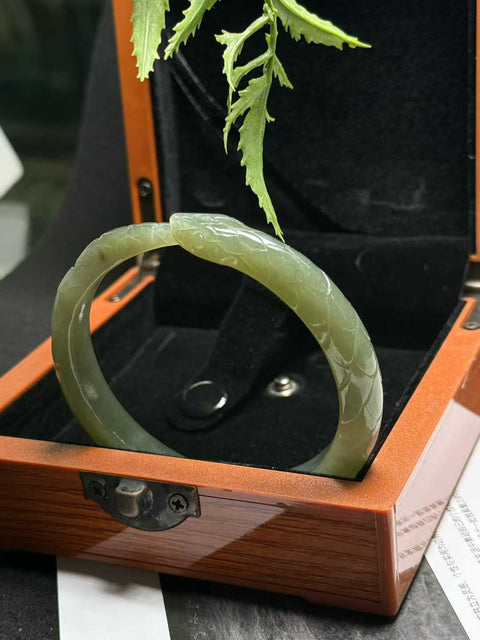 "Gelang Ular" giok Hetian ini memiliki rona hijau danau dan tekstur lembut yang hangat. Desain ukiran tangan yang tampak nyata. Perkiraan dimensi: 58 x 10 mm. Semua barang terbuat dari batu alam; biaya kirim dan pajak sudah termasuk.