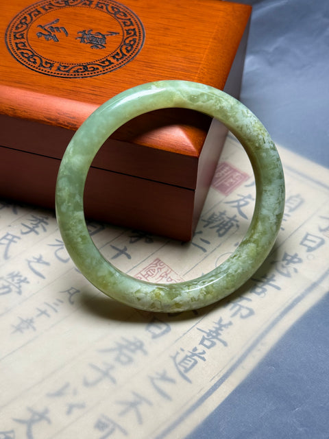 Gelang giok Xiuyan alami, dihiasi dengan desain yang disebut "Kekayaan Tak Tertandingi." Perkiraan dimensi: 62×11,8×8,9 mm. Semua batu terbentuk secara alami; termasuk ongkos kirim dan pajak.
