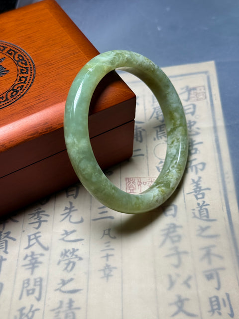 Gelang giok Xiuyan alami, dihiasi dengan desain yang disebut "Kekayaan Tak Tertandingi." Perkiraan dimensi: 62×11,8×8,9 mm. Semua batu terbentuk secara alami; termasuk ongkos kirim dan pajak.
