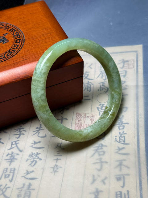 Gelang giok Xiuyan alami, dihiasi dengan desain yang disebut "Kekayaan Tak Tertandingi." Perkiraan dimensi: 62×11,8×8,9 mm. Semua batu terbentuk secara alami; termasuk ongkos kirim dan pajak.