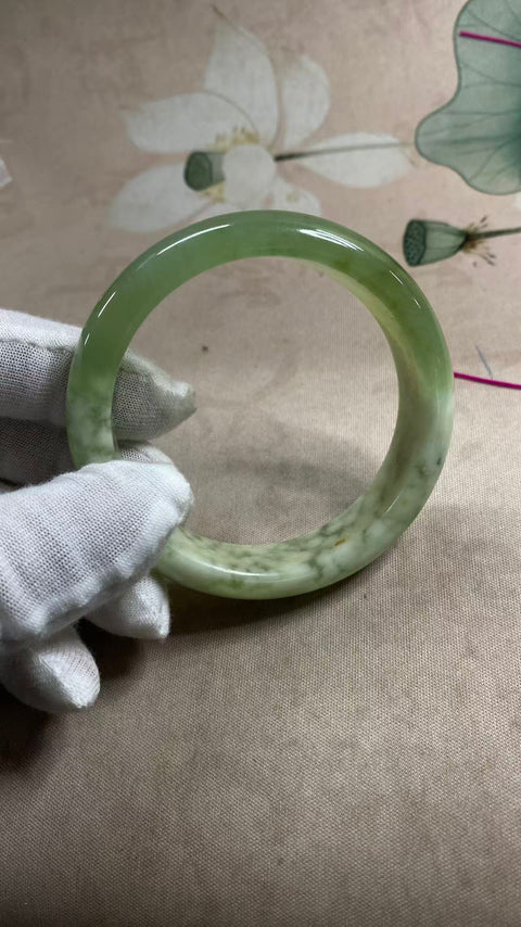 Gelang giok Xiuyan yang indah dengan rona hijau dan tekstur seperti susu, setengah giok dan setengah hijau, berdiameter 57,6 mm dan lebar 14,5 mm. Semua batu terbentuk secara alami; polanya acak. Biaya pengiriman dan pajak sudah termasuk