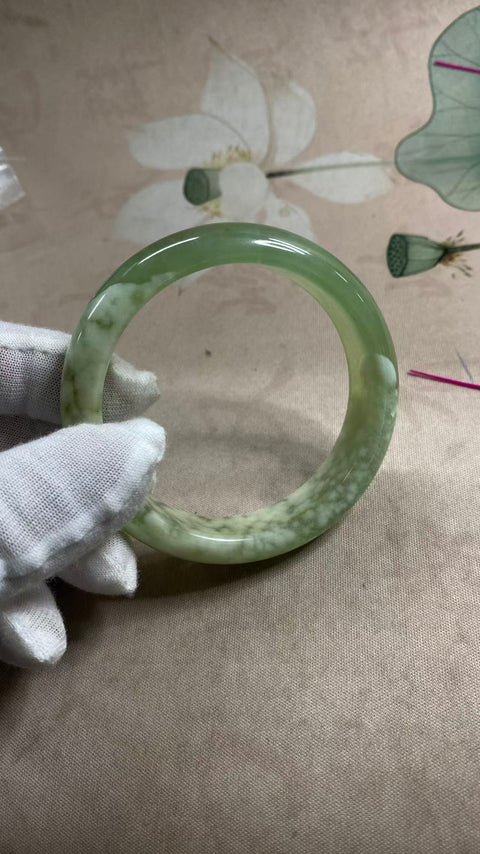 Gelang giok Xiuyan yang indah dengan rona hijau dan tekstur seperti susu, setengah giok dan setengah hijau, berdiameter 57,6 mm dan lebar 14,5 mm. Semua batu terbentuk secara alami; polanya acak. Biaya pengiriman dan pajak sudah termasuk